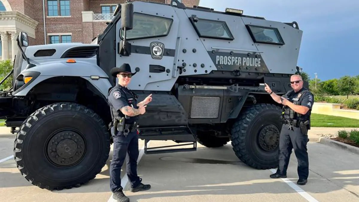 Two Prosper Police officers pointing at the department's grey armored vehicle.